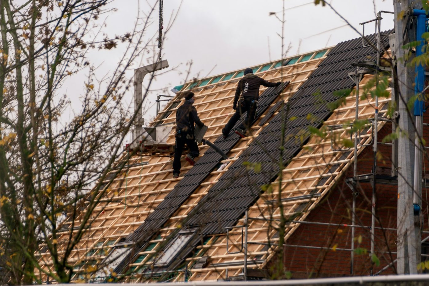 Two workers installing dark shingles on a steep roof with scaffolding
